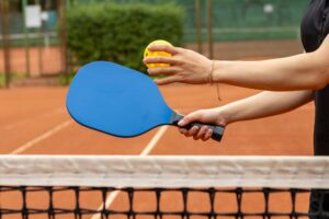 Two players engage in a tennis-table game, one holding a blue paddle and the other about to hit a yellow ball near the net.