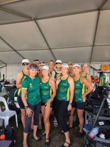 Group of women athletes in matching green and yellow uniforms posing together under a large white event tent.