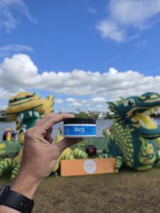 Hand holding a blue-lidded jar in the foreground, festival dragon decorations in the background.