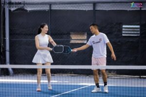Two players on a blue indoor tennis court shake hands over the net after a match.